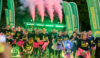 A large group of people taking part in a night-time fun run. Many of them are wearing brightly coloured tuts, face paints and glowsticks.