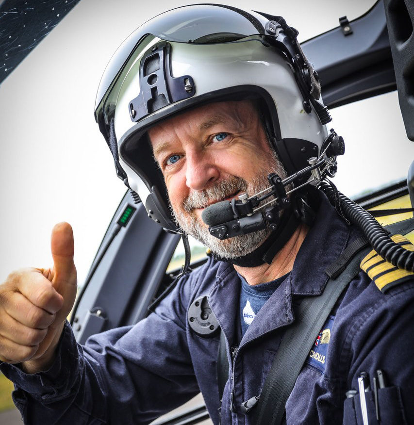 Pilot Dave is sitting in the helicopter wearing his blue flight suit and a flight helmet and is giving you a thumbs up!