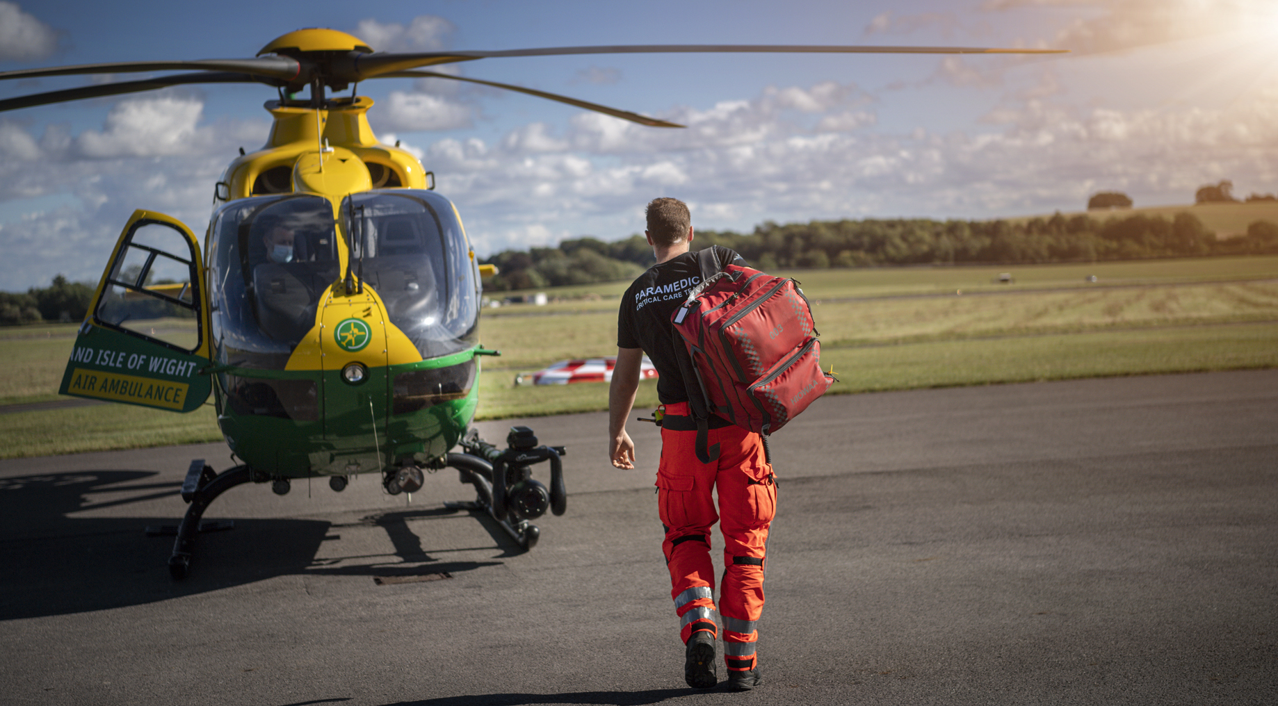 HEMS Paramedic Jason has his back to the camera and is walking towards the helicopter. Jason is carrying a kit bag.