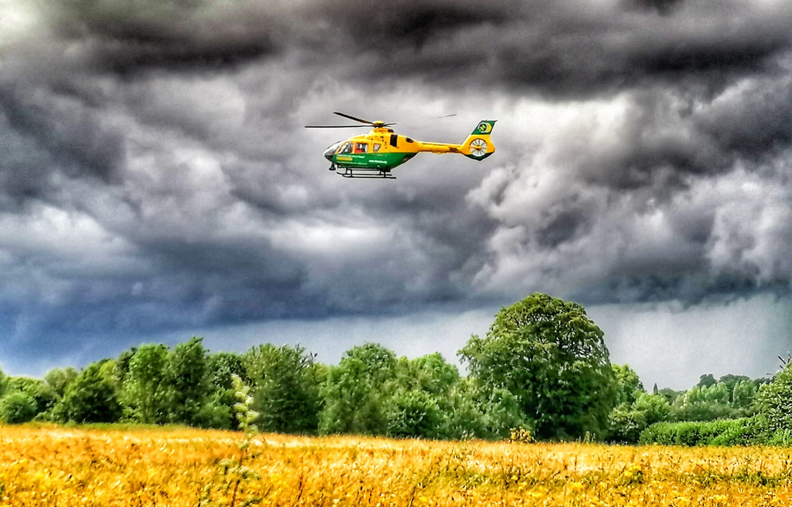 Helicopter flying above a field with an overcast sky