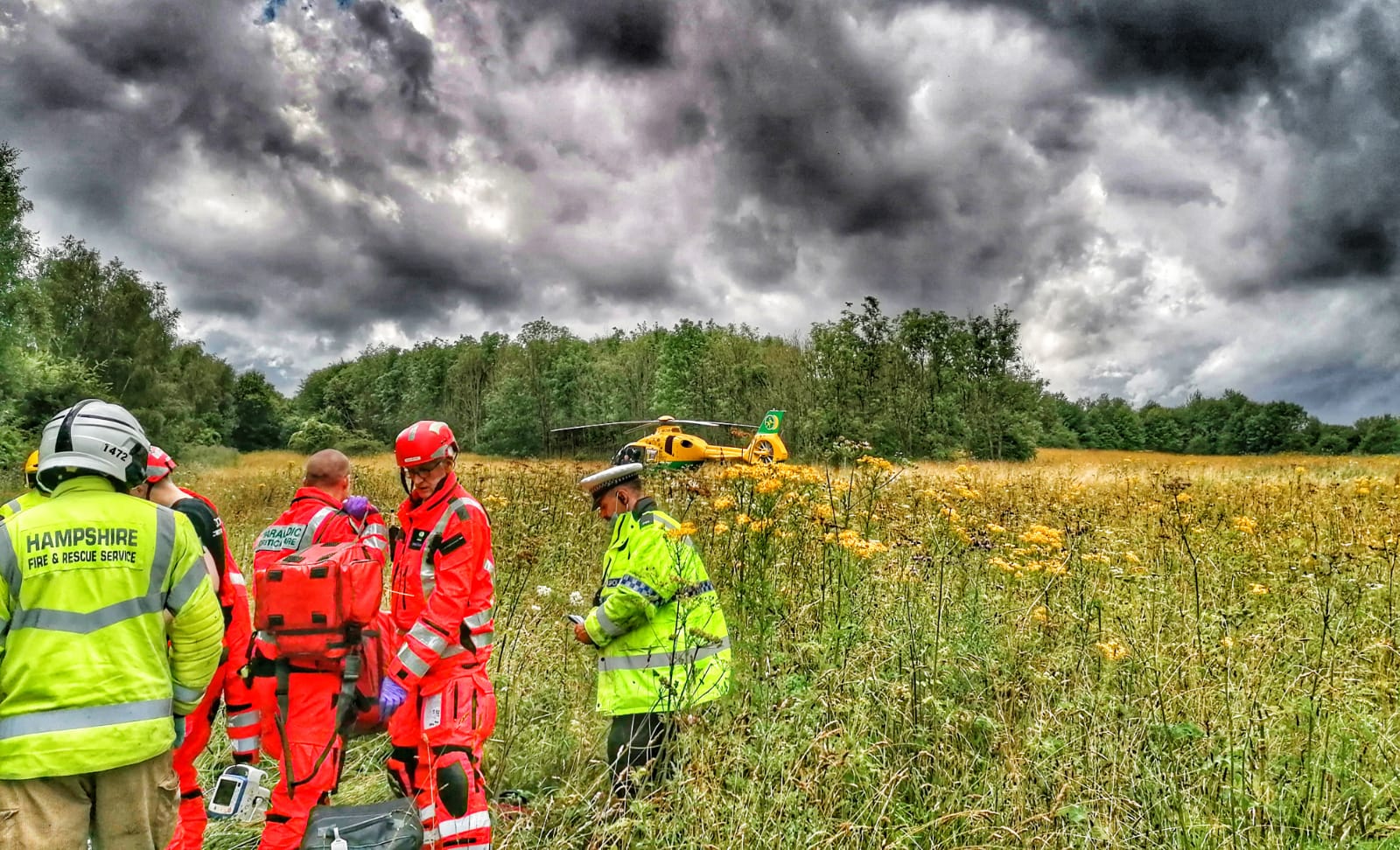 A team of paramedics, doctors, police and fire service in a field with a helicopter in the background