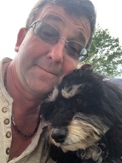 A man with a dog and a tree in the background