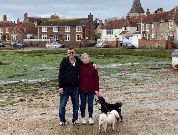 A man and a lady stood on a beach with their two dogs
