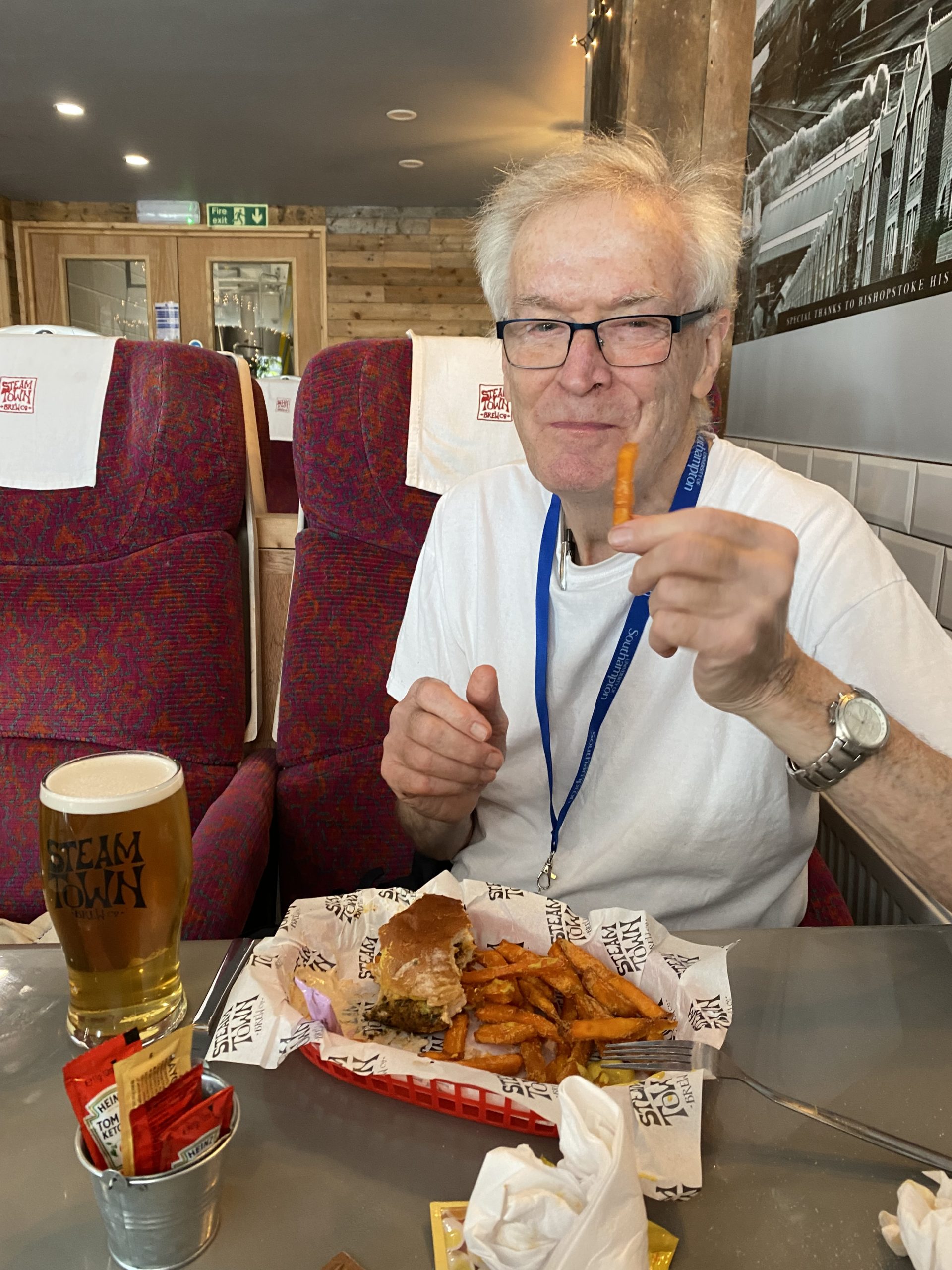 A man sat in a restaurant or diner with a burger and chips and a pint of beer
