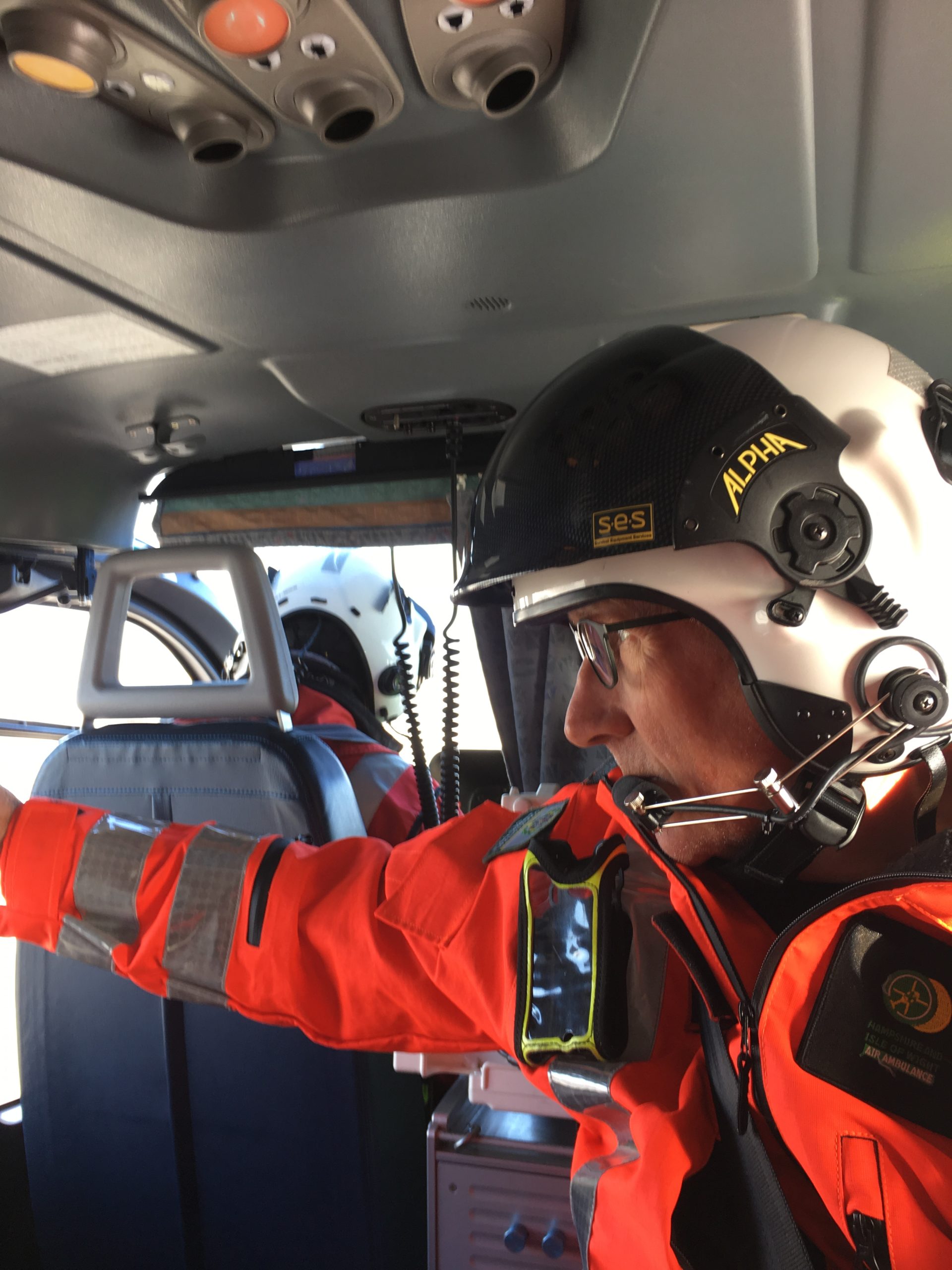 A man wearing a flight helmet looking to the side with his right arm stretched out