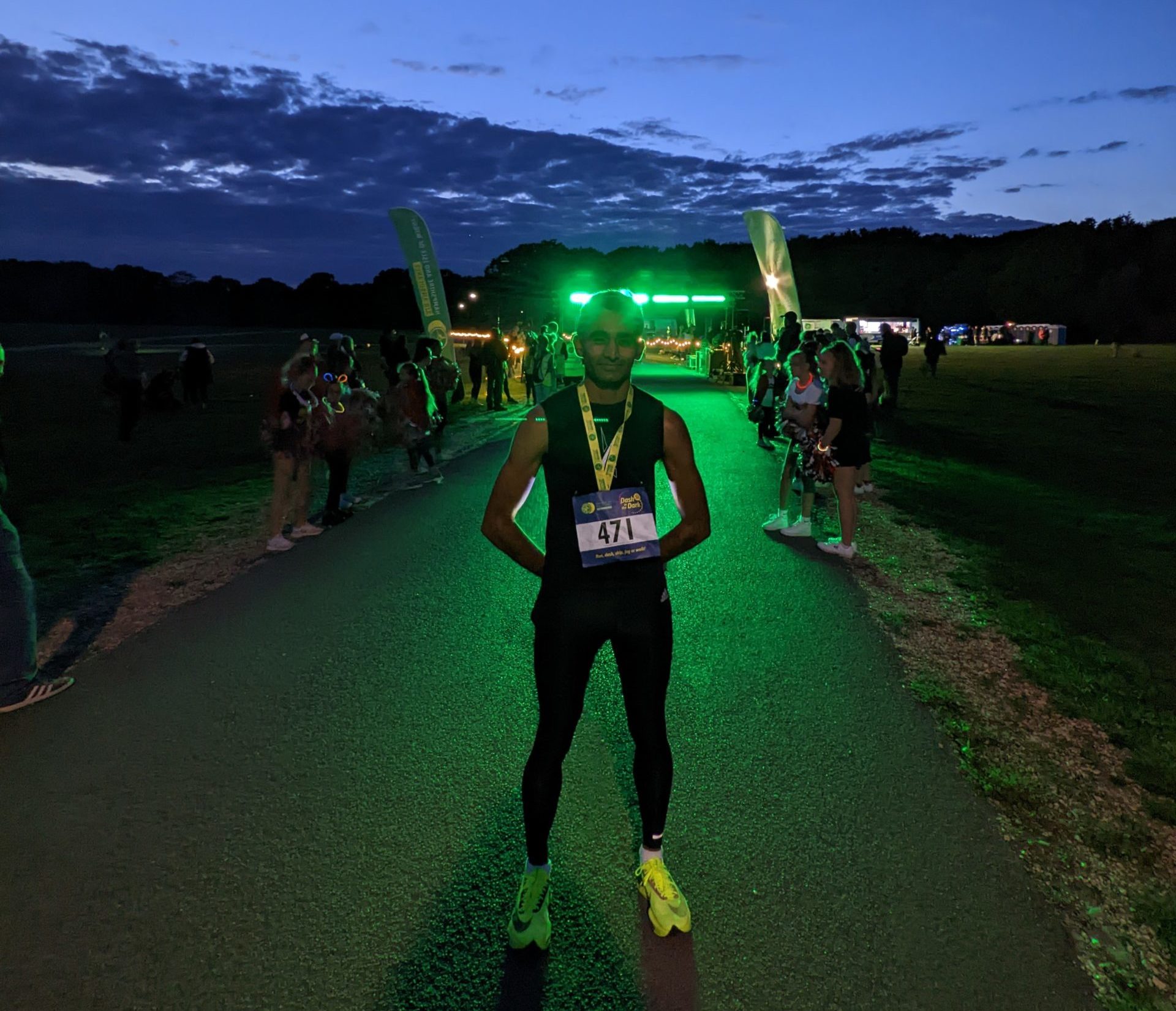 A man stood at the finish line of a race with green lights in the background
