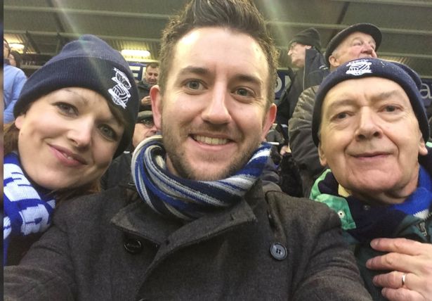 Three people at a football match smiling at the camera