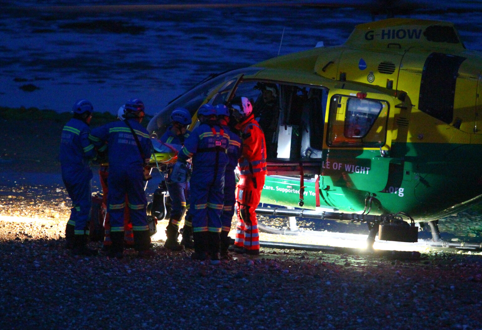 A team of medics loading a patient onto a helicopter that has landed on a beach at night