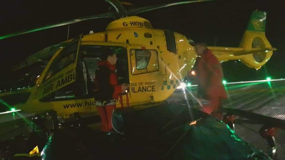 A patient on a trolley in front of a yellow helicopter at night