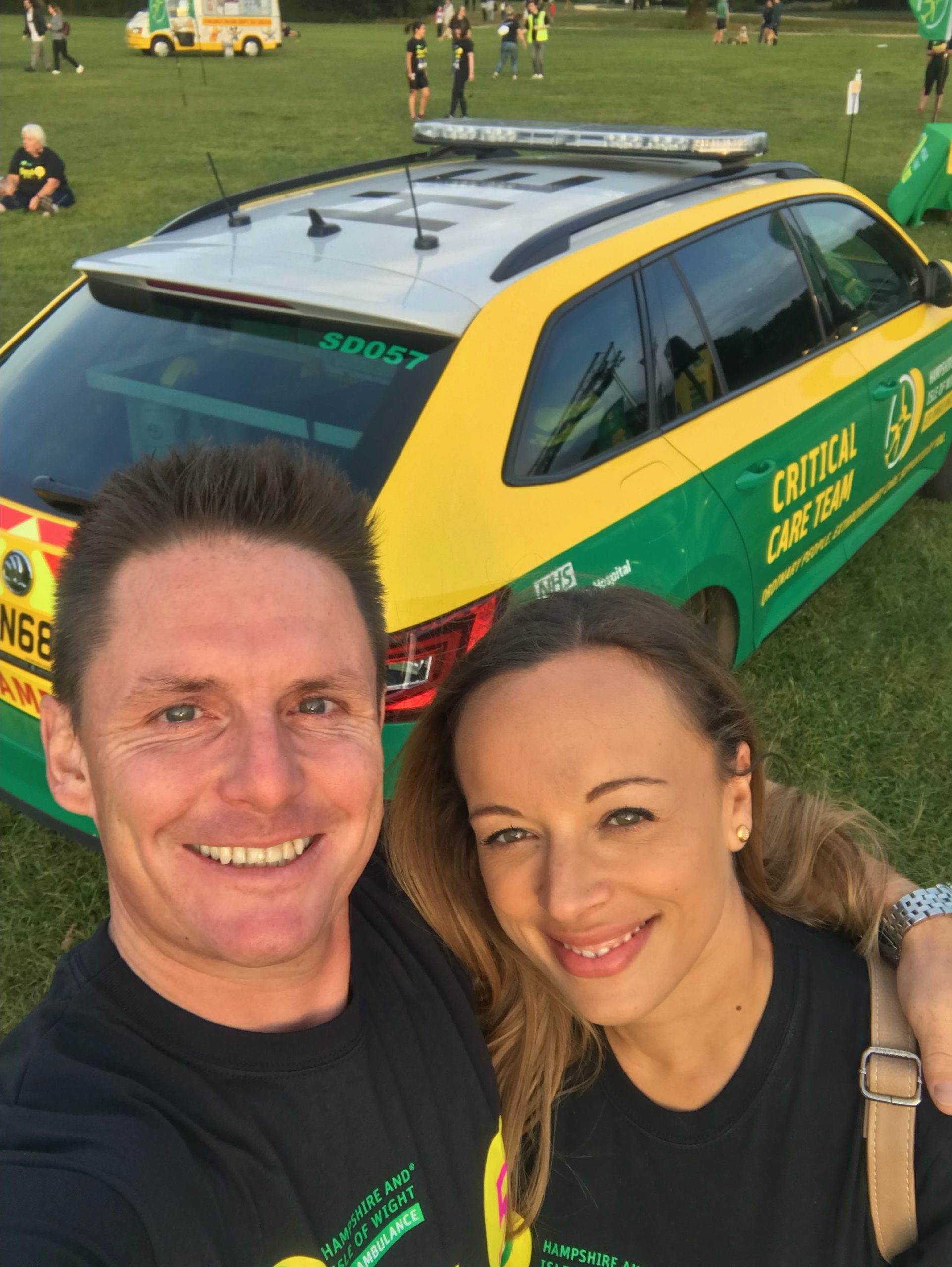 A man and a woman smiling with an emergency vehicle parked behind them