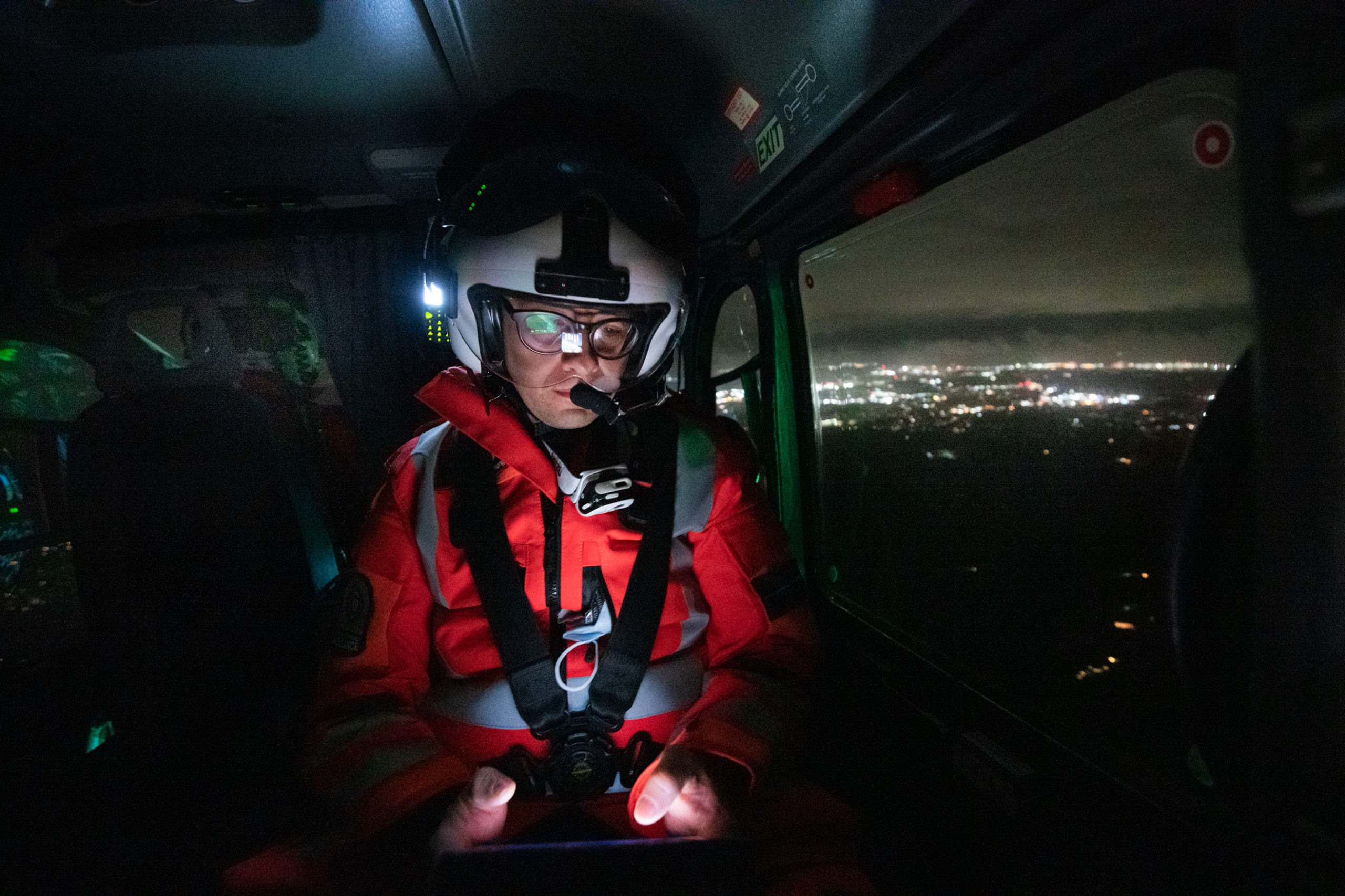 A doctor sat in the back of a helicopter at night with city lights in the background.