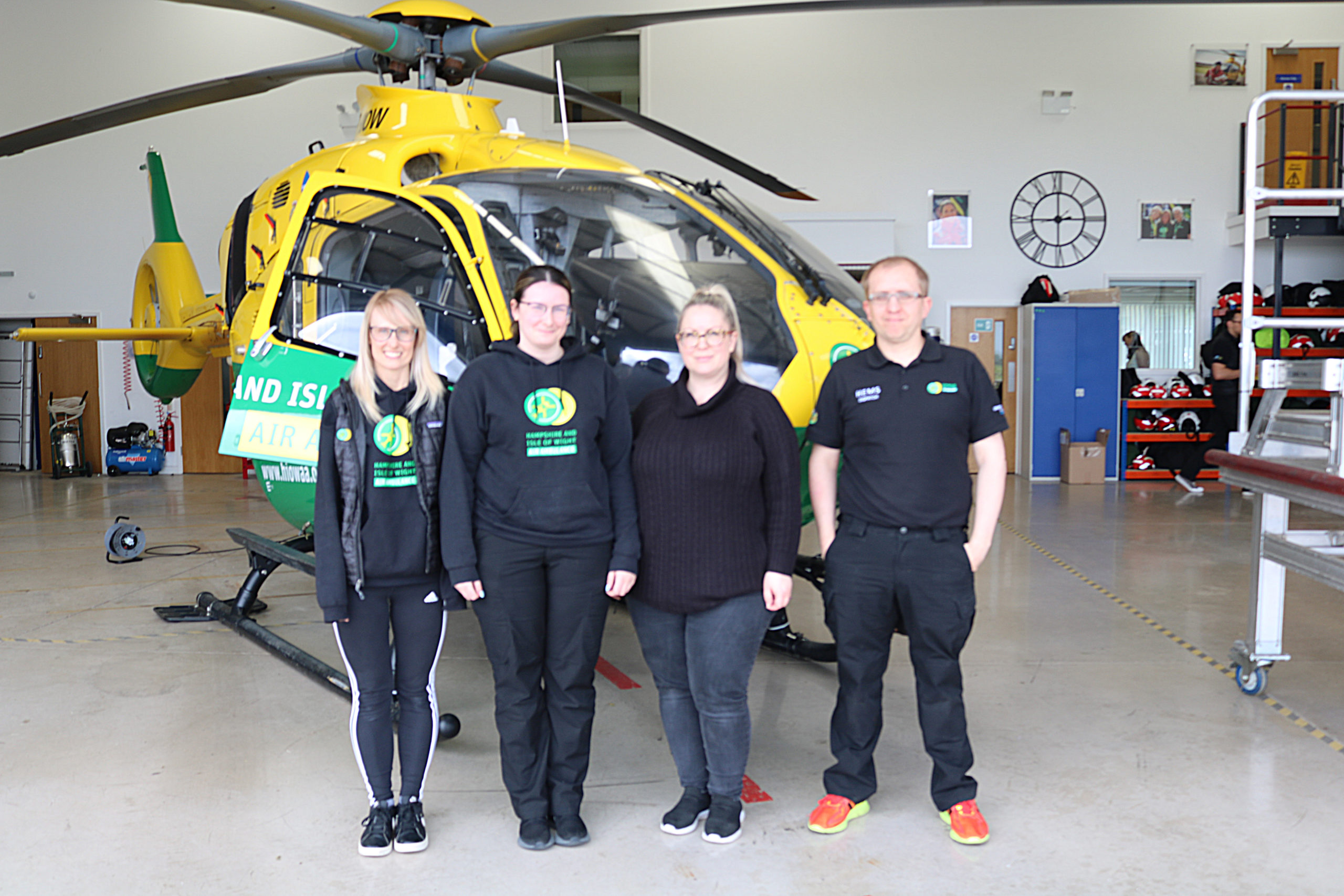 Four dispatchers standing in front of a helicopter inside an aircraft hangar.