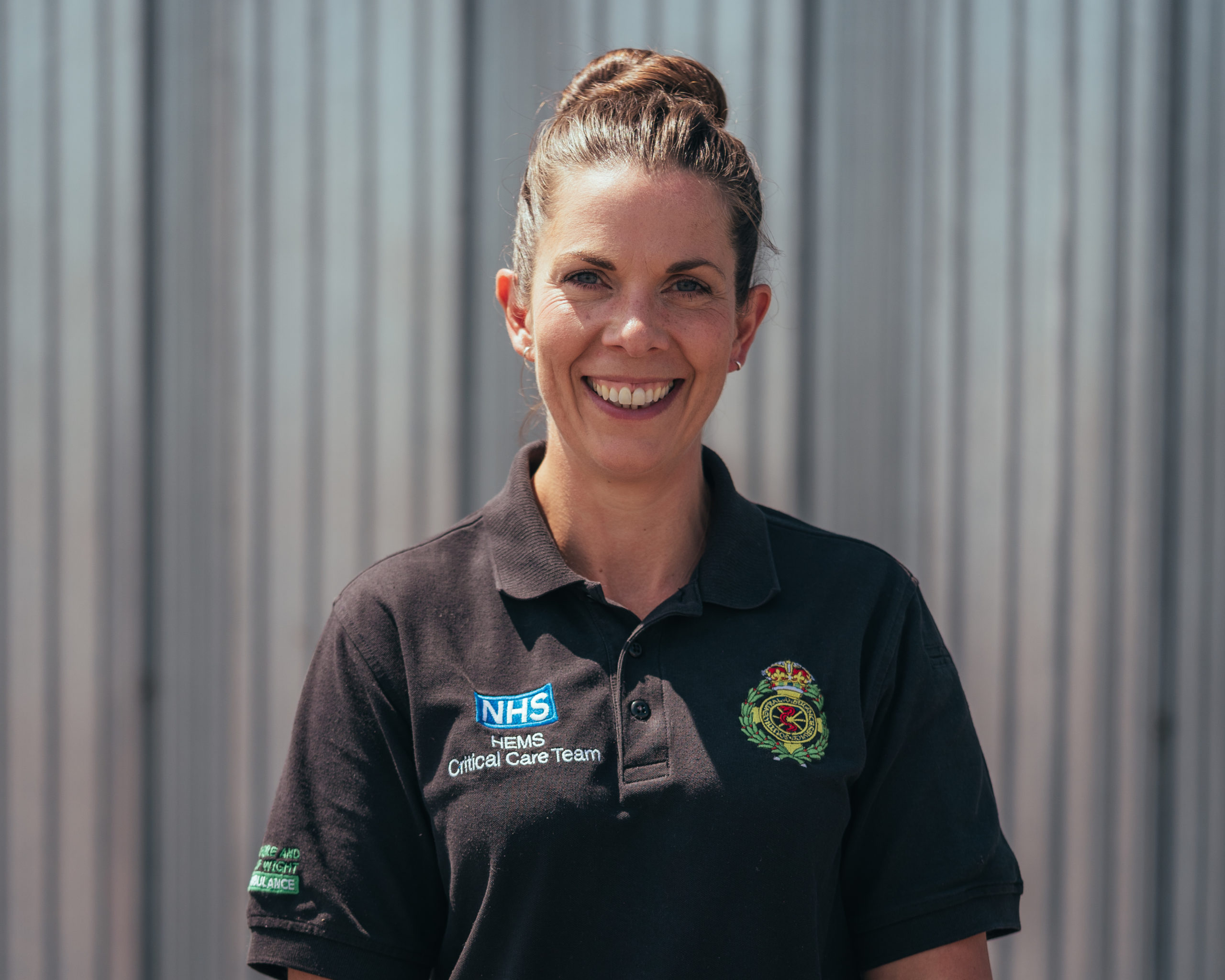 Nicola Hawkes is smiling to the camera. She is stood outside the airbase hangar in the sunshine.