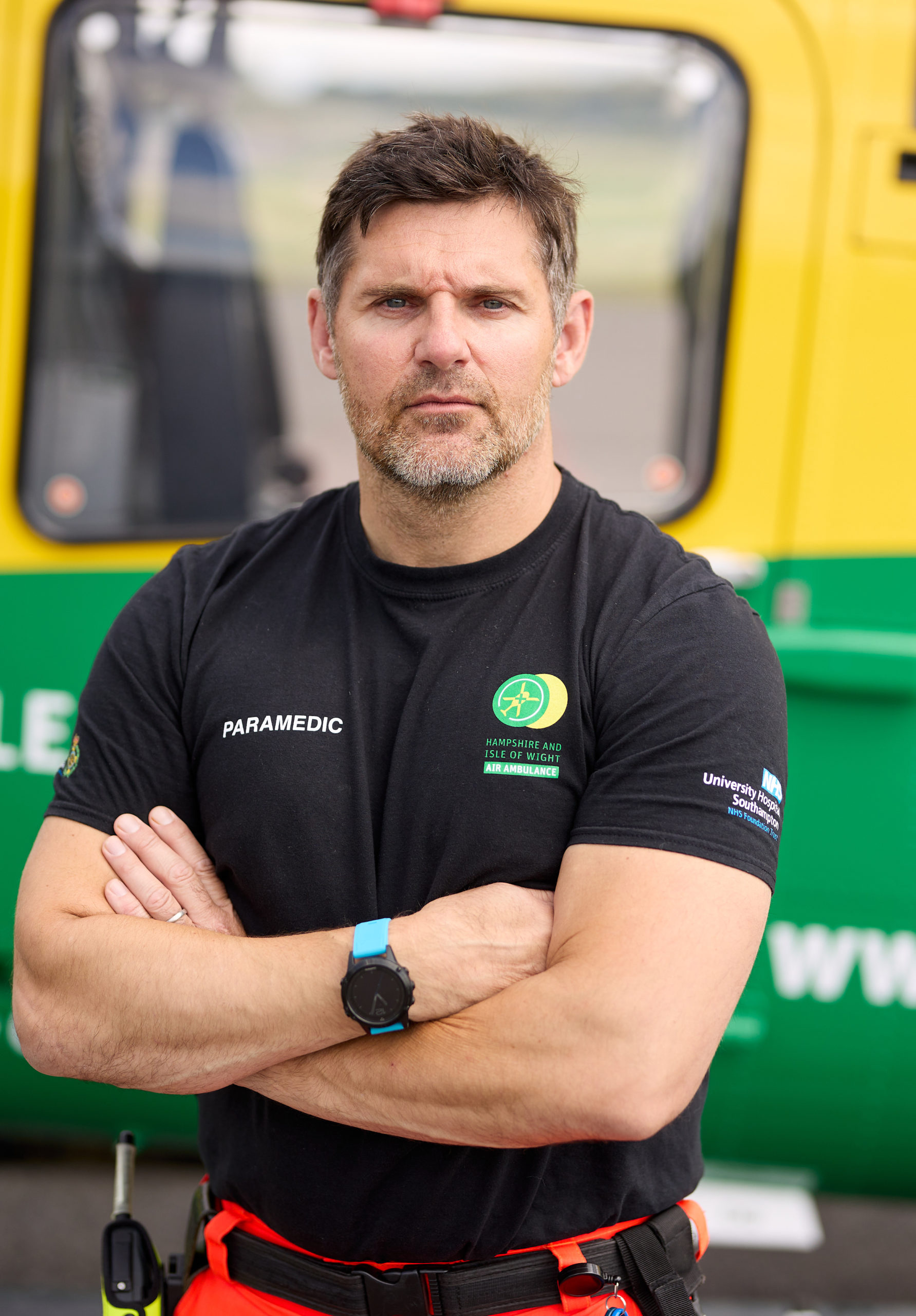 Specialist Critical Care Paramedic John Gamblin is standing in front of the helicopter with his arms crossed. He is looking at the camera.