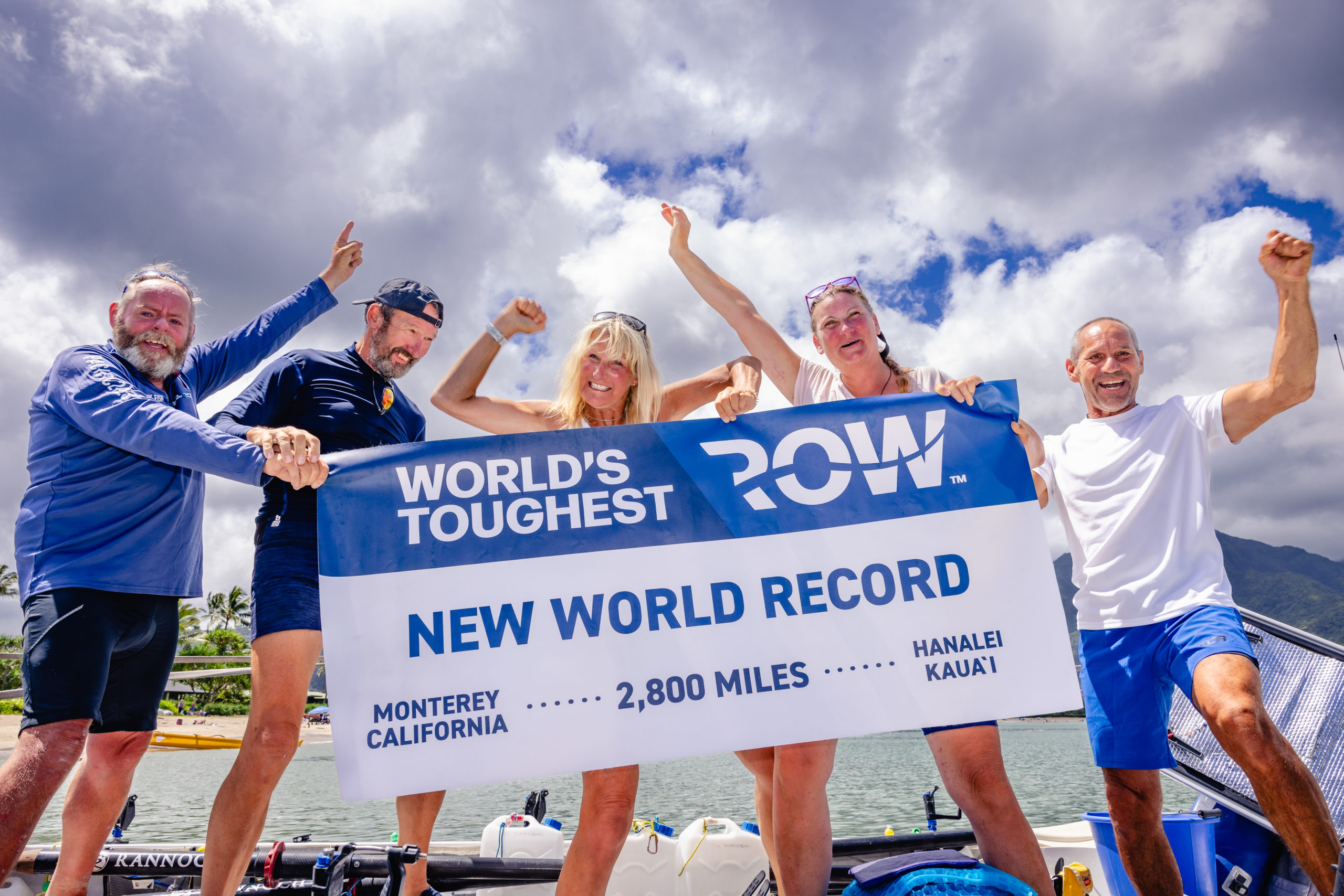 Five people holding a banner marking the completion of the world's toughest row.