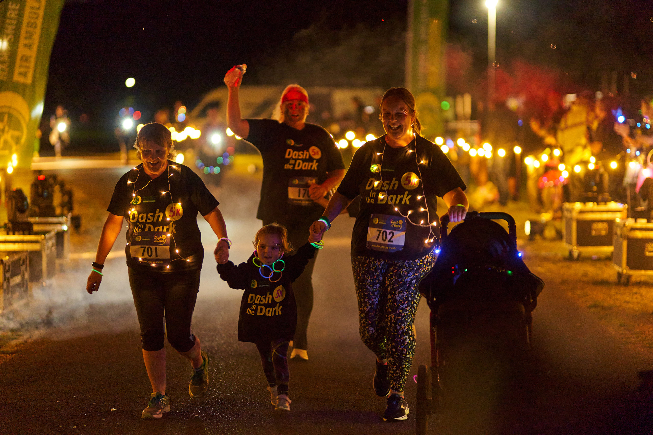 Four people draped in lights on a fun run - one lady pushing a child's buggy