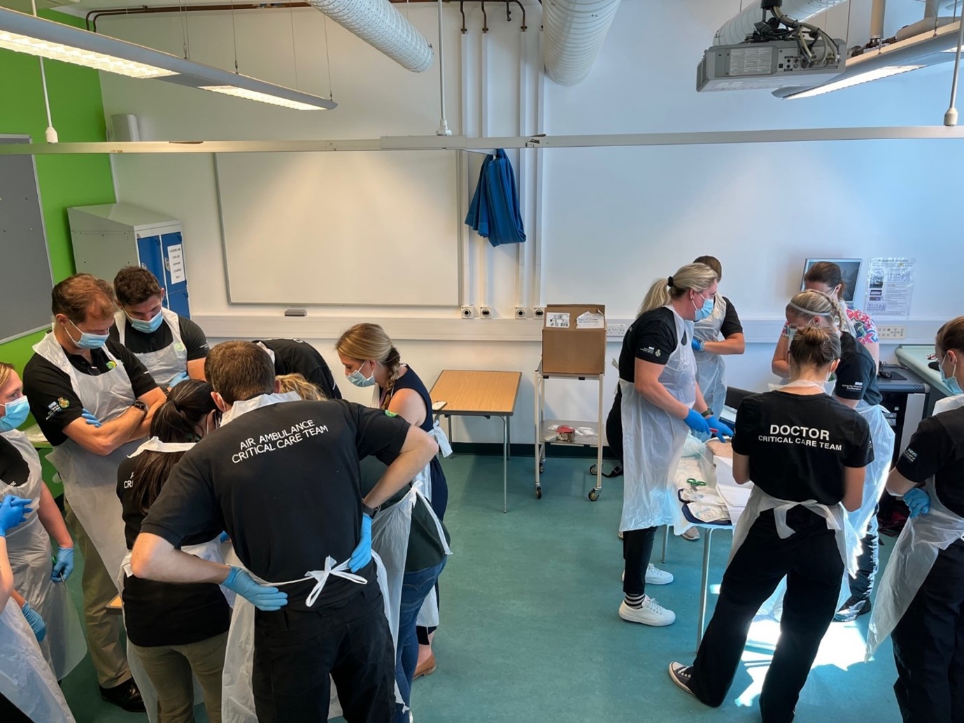 A room of people carrying out surgical procedures on two manikins in a training scenario.