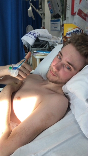 A man lying in a hospital bed with his thumb up