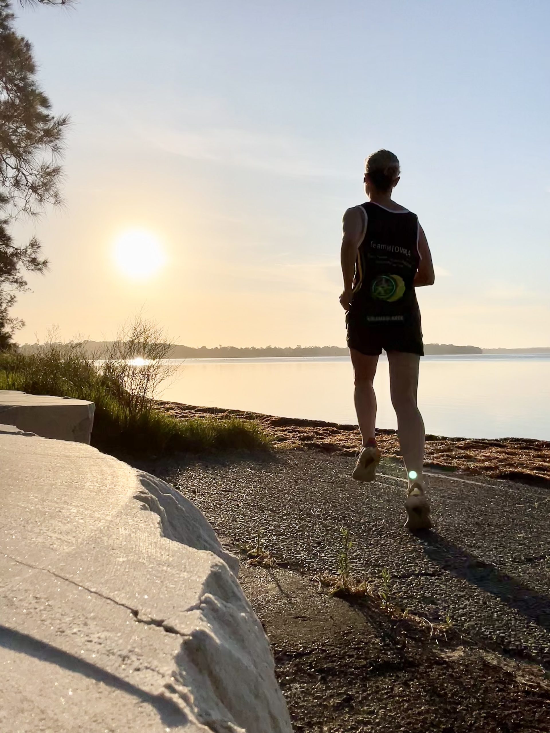 A lady running along the coast with the sun in the background