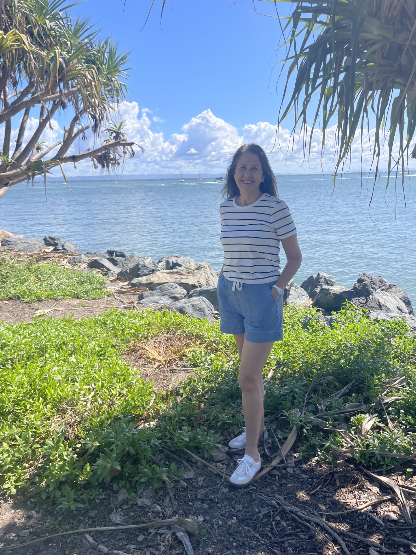 A lady stood on the coast with the sea and blue skies behind her.