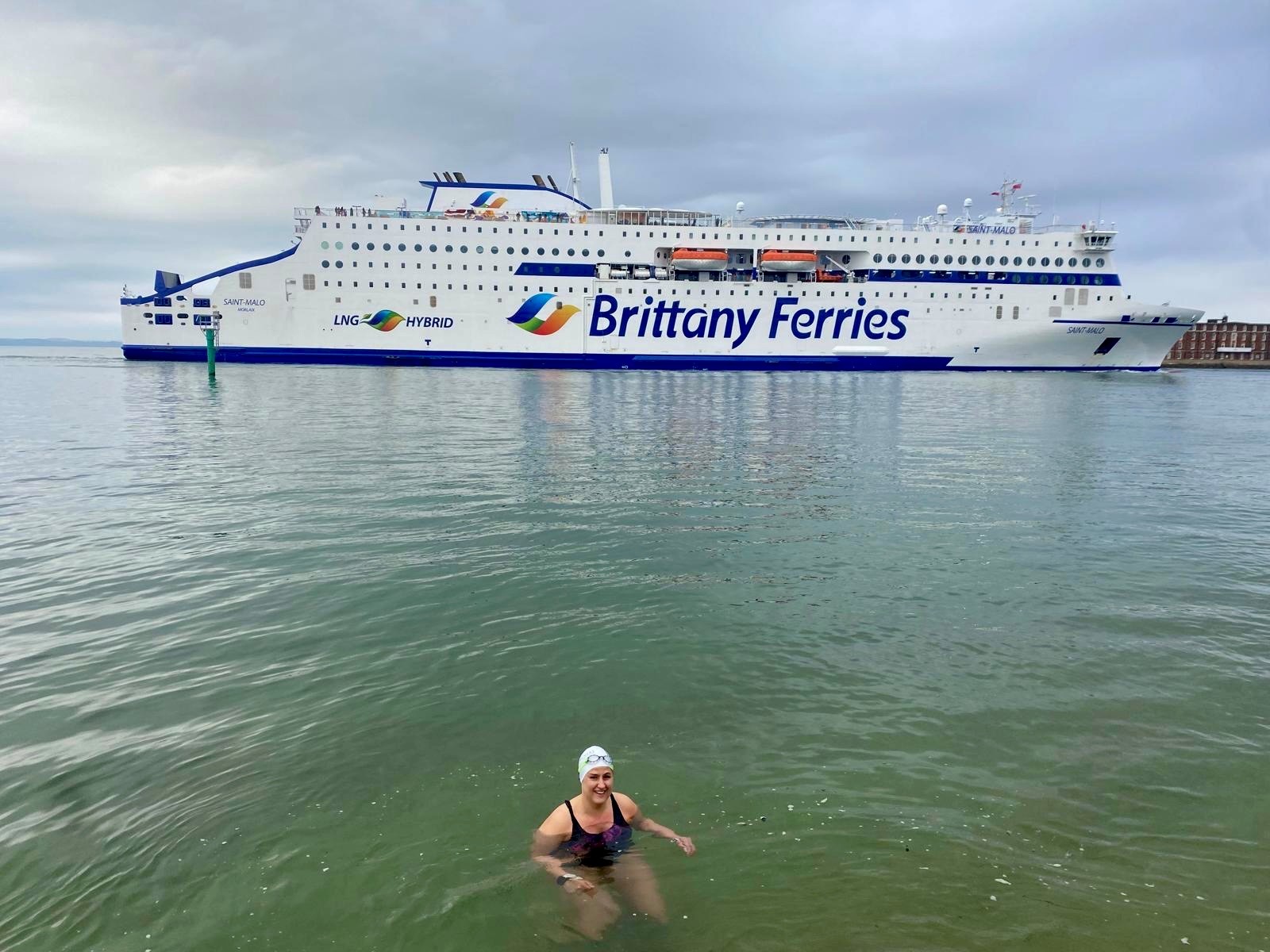 A lady open water swimming. There is a large white ferry in the background.