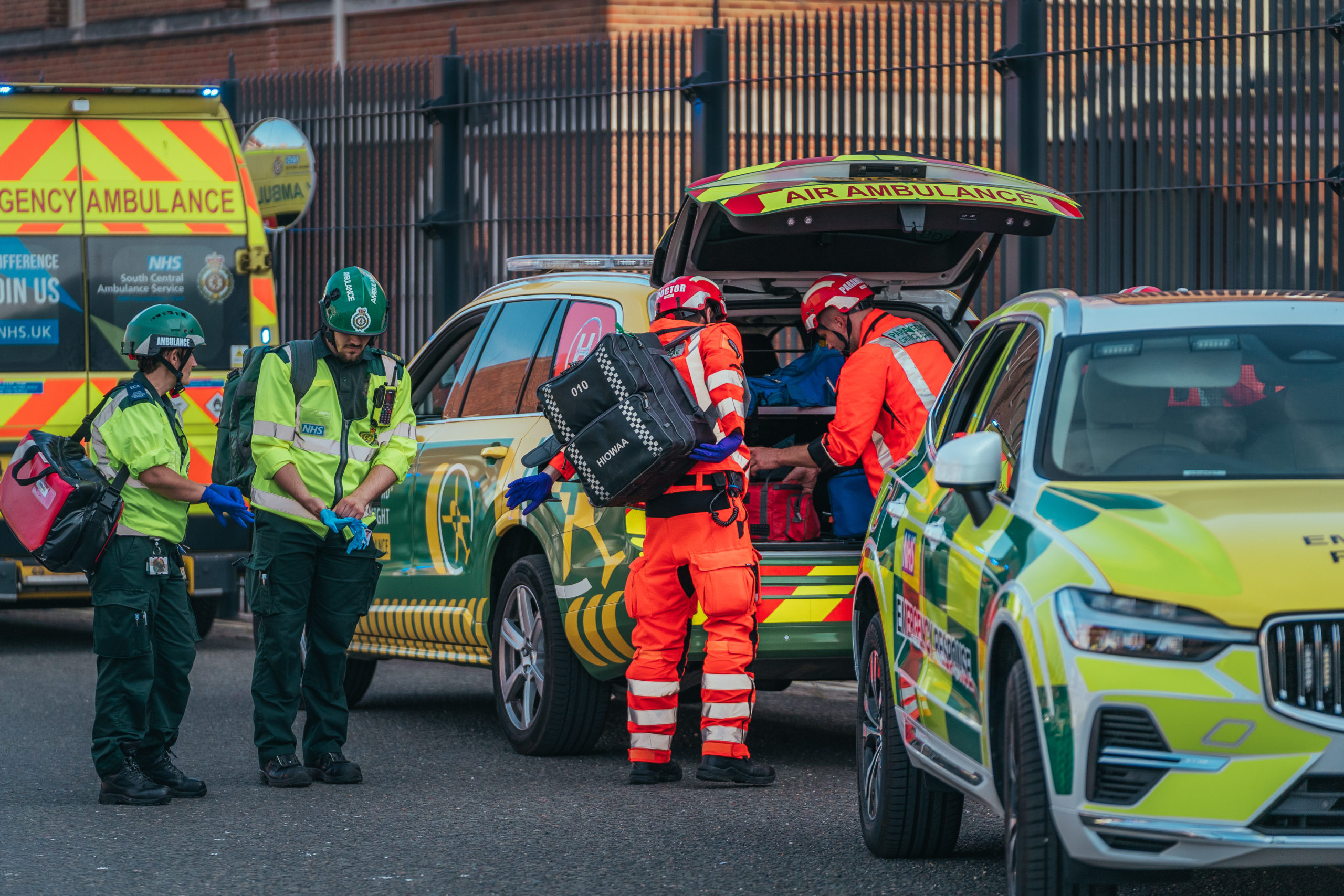 Crew preparing their kit from the boot of the Emergency Response Vehicle in a busy emergency scene. There are other ambulances and paramedics on scene as well.