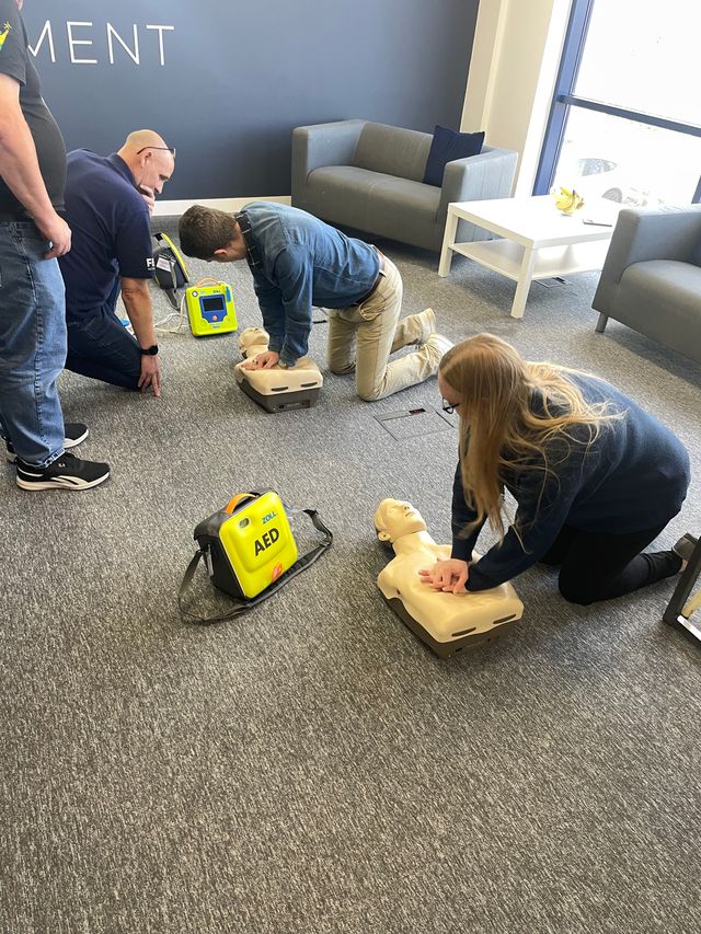 Two people are performing CPR on a training manikin in an office building.