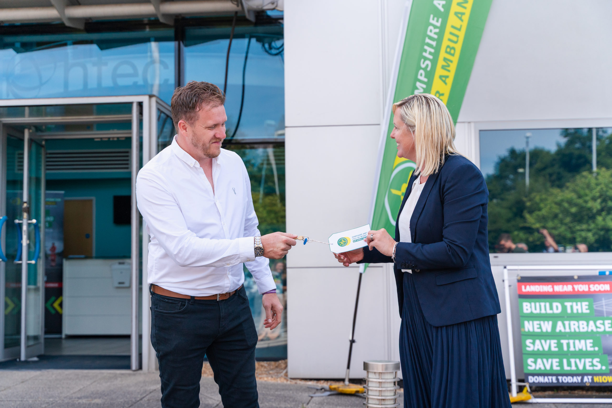Two people stood in front of a large building. They are doing a key handover ceremony.