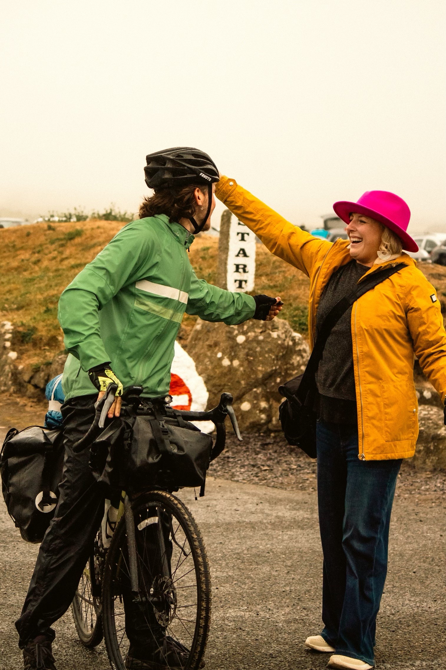 A lady and her son (the son is on a bicycle) about to hug one another. The lady is smiling at him.