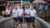 Four people stood on a bridge with a crowd of people cheering in the background.