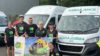 A group of people wearing HIOWAA cycling tops stood in front of an ambulance holding a HIOWAA flag.