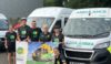A group of people wearing HIOWAA cycling tops stood in front of an ambulance holding a HIOWAA flag.
