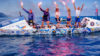 Five rowers stood on a vessel holding red flares above their heads.