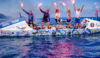 Five rowers stood on a vessel holding red flares above their heads.