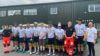 A group of cyclists and two paramedics standing in a line in front of an emergency response vehicle.