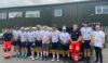 A group of cyclists and two paramedics standing in a line in front of an emergency response vehicle.