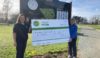 Two people holding a large cheque in front of a golf club sign.