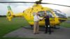 A pilot and Chairman shaking hands and holding the key to the helicopter they are standing in front of.