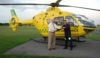 A pilot and Chairman shaking hands and holding the key to the helicopter they are standing in front of.