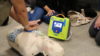 A person performing chest compressions on a manikin that is strapped up to a defibrillator
