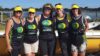 A team of six rowers standing in front of a boat.