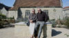 Two people sat on a brick and concrete structure in front of a small church.