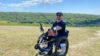 Dale on a practice climb. The sun is shining and he is up a hill. He has yellow ropes in front of him to help people pull him up in his wheelchair.