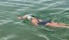 A person open water swimming. She is wearing a white swim cap with Hampshire and Isle of Wight Air Ambulance emblazoned on it.