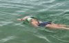 A person open water swimming. She is wearing a white swim cap with Hampshire and Isle of Wight Air Ambulance emblazoned on it.