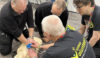 Volunteer teaches a group how to perform successful CPR on a manikin