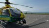 A helicopter landed in an empty car park. The sea and blue clouds are in the background.