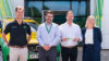 A group of people standing in front of a building and a green and yellow emergency response vehicle. They are doing a key handover to the building.
