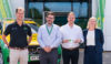 A group of people standing in front of a building and a green and yellow emergency response vehicle. They are doing a key handover to the building.
