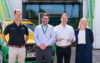 A group of people standing in front of a building and a green and yellow emergency response vehicle. They are doing a key handover to the building.
